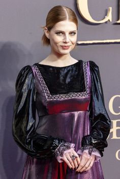 a woman in a purple and black dress standing on a red carpet with her hands in her pockets