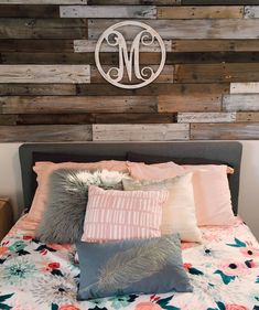 a bed topped with lots of pillows next to a wall mounted monogrammed sign