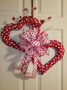 a red and white heart shaped wreath hanging on the front door with polka dot ribbon