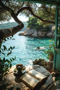 an open book sitting on top of a wooden table next to a tree and water