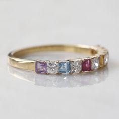 a yellow gold ring with multicolored stones on it's sides, sitting on a white surface