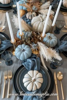 the table is set with blue and white pumpkins, silver candlesticks, feathers, and other decorative items