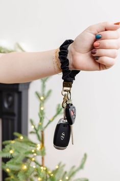 a woman's hand holding two car keys in front of a christmas tree