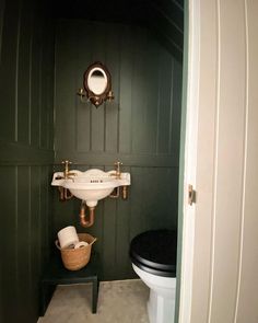 there is a bathroom with green walls and white fixtures on the wall, along with a black toilet