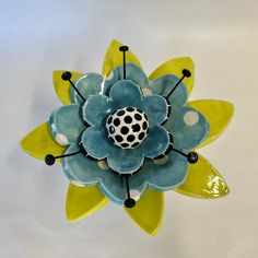 a blue and yellow flower with black dots on it's center piece, sitting on a white surface