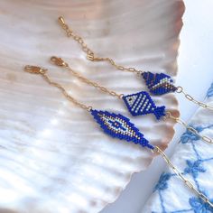 three blue and white beaded fish earrings on a gold plated chain, resting on a seashell