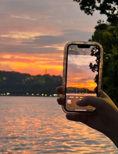 a person holding up a cell phone in front of a body of water at sunset