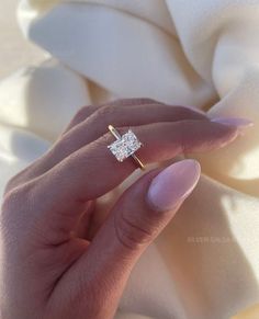 a woman's hand with a diamond ring on top of her finger, in front of a white blanket