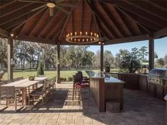 an outdoor kitchen and grill area with lights on the ceiling, surrounded by brick pavers