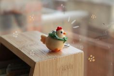 a small toy chicken sitting on top of a wooden table next to a glass window