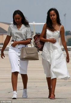 two women in white dresses walking down the runway with one holding a purse and another carrying a handbag