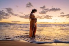 a pregnant woman standing in the ocean at sunset with her belly wrapped up and wearing a flower crown