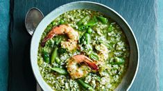 a bowl filled with shrimp and rice on top of a blue table next to a spoon