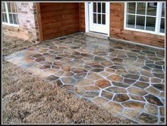 a stone patio in front of a house with wood siding and white doors on the side