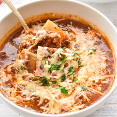 a bowl of chili soup with cheese and meat on the side, being held up by a spoon