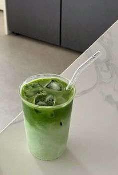 a green drink with ice and lime slices in it sitting on a white counter top