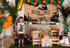 a young boy standing in front of an assortment of items on display at a dinosaur birthday party