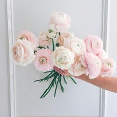 a bouquet of pink and white flowers is held by someone's hand in front of a door