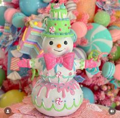 a snowman with a green hat and pink bow tie sitting on top of a cake