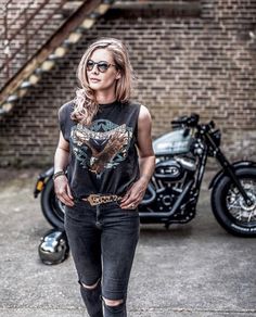 a woman standing in front of a motorcycle wearing sunglasses and a t - shirt with an eagle on it