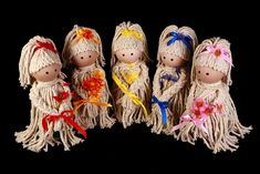 five little dolls are lined up together on a black background, one is wearing a dress and the other has flowers in her hair