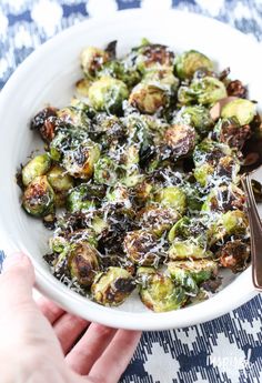 a white bowl filled with brussel sprouts and topped with parmesan cheese