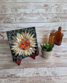 there is a potted plant next to a small mosaic on the table with two bottles