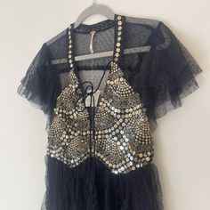 a black top with sequins and beads hanging on a hanger in front of a white wall