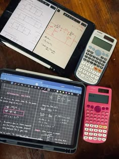 three calculators sitting next to each other on top of a wooden table in front of an open notebook