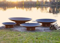 four black plates sitting on top of a grass covered field next to a lake with trees in the background