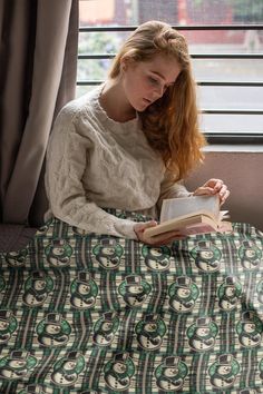 a woman reading a book while sitting on a bed in front of a large window