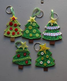 four christmas trees made out of felt and buttons on a gray surface, with one keychain in the shape of a tree