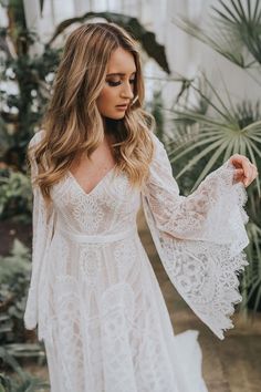 a woman wearing a white lace dress with long sleeves and an open - back design