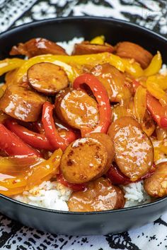 a black bowl filled with rice covered in sausages and peppers on top of it