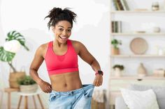 a woman in a pink sports bra top and blue jeans is holding up her pants