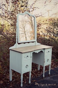 an old vanity with a mirror on it in front of some bushes and trees,