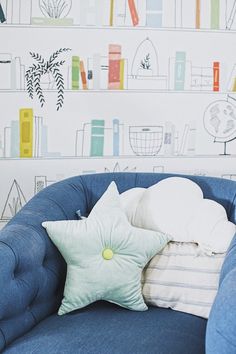 a blue chair with pillows on it in front of a wallpapered bookcase