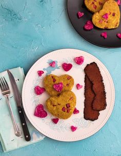 two heart shaped cookies are on a plate next to a piece of cake and a fork