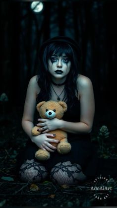 a woman holding a teddy bear sitting in the dark with her hands on her chest