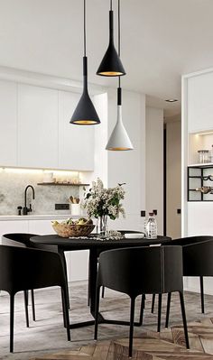 a dining room table with chairs and lights hanging from it's ceiling in front of an open kitchen