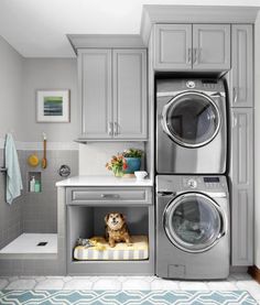 a washer and dryer in a small room with grey cabinets, white counter tops and blue rug