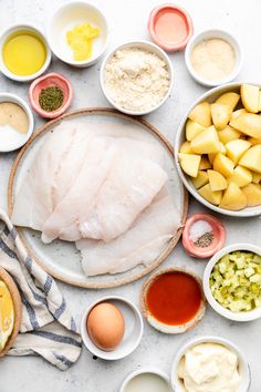 an assortment of ingredients are laid out on a white counter top, including fish and potatoes