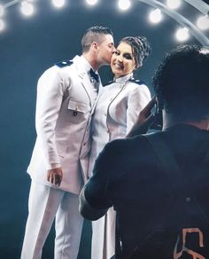 a man and woman are kissing in front of a mirror with lights on the wall behind them