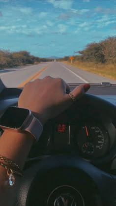 a person is driving on the road with their hand on the steering wheel while wearing an apple watch