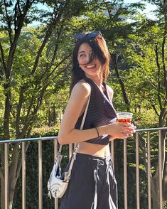 a woman standing next to a metal fence holding a cup in her hand and smiling at the camera