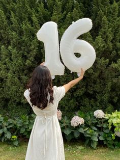 a woman in a white dress holding up an air filled number six balloon