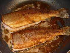 two fish cooking in a frying pan with sauce on the bottom and one being cooked