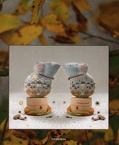 two small ceramic figurines sitting on top of each other in front of leaves