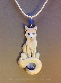 a necklace with a white fox sitting on it's side and a blue bead around the neck