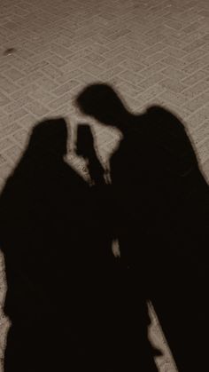 the shadow of two people standing next to each other with their cell phones in their hands